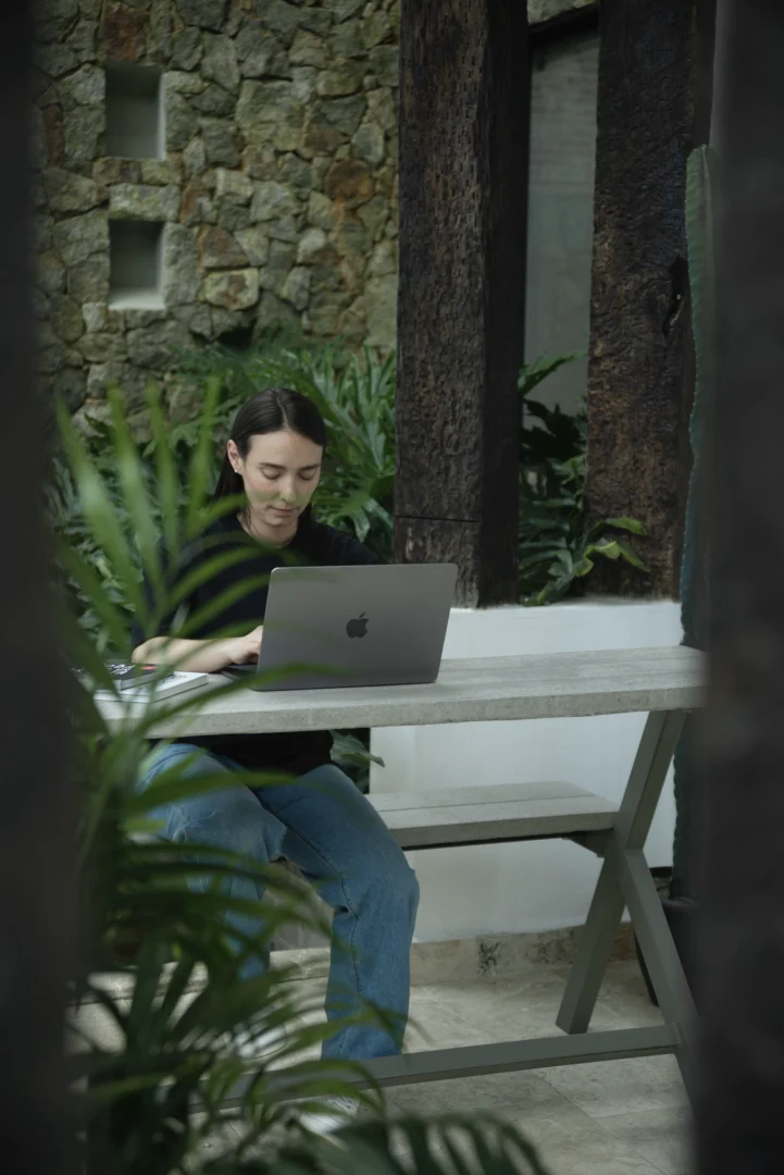 Persona trabajando con su computador portátil al aire libre en una mesa picnic de concreto